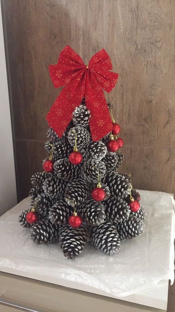 A cone shaped Christmas tree made of snowy pinecones, decorated with red ornaments and topped with a red bow