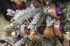 a flocked Christmas tree with purple and gold glitter ornaments, gilded pinecones, lights and copper disco balls