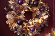 a refined Christmas wreath of gilded and dark leaves, purple ornaments, pinecones, lights and faux berries is fantastic idea
