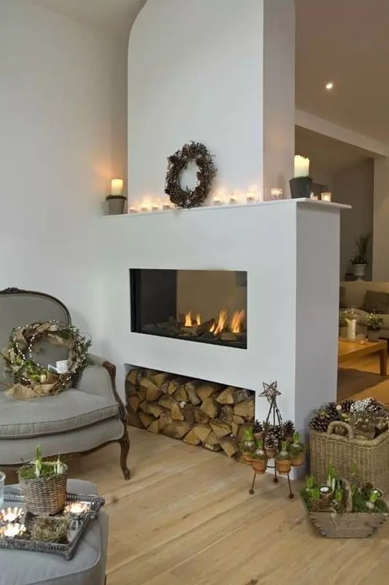 a sleek white fireplace with firewood storage, candles on the mantel and a wreath with pinecones for winter