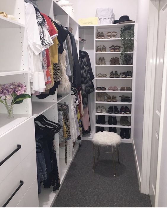 a small white closet done with IKEA storage units, open shelves, storage compartments and railings, a white faux fur stool