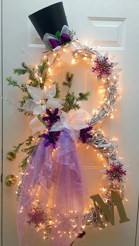 a snowman shaped Christmas wreath with lights, with a gold monogram, a top hat, lights, evergreens and touches of purple