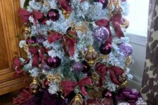 a sophisticated flocked Christmas tree with purple, clear and purple print ornaments, purple and gold ribbon bows