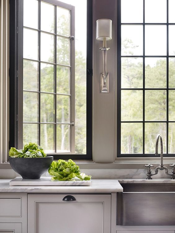an English country kitchen with a white stone countertop, chic French-style casement windows and elegant lamps