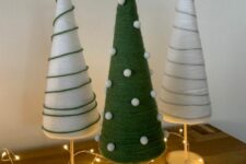 white and green yarn cones decorated with threads and white pompoms, topped with white stars and decorated with lights