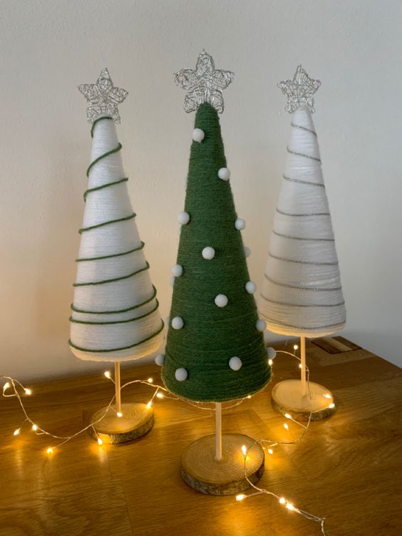 white and green yarn cones decorated with threads and white pompoms, topped with white stars and decorated with lights
