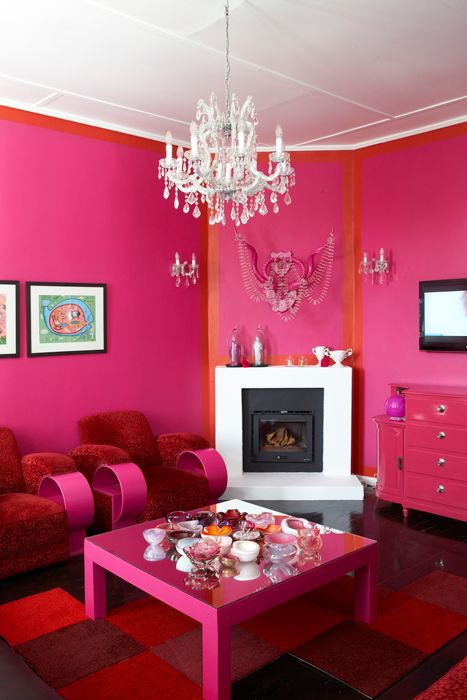 A magenta and orange living room with a built in fireplace, red and pink furniture, a crystal chandelier and a bold rug
