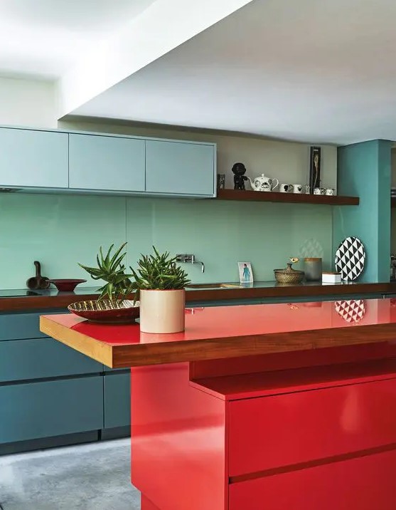 a minimalist kitchen with blue and muted blue cabinets, a mint green backsplash, a bold red kitchen island and wooden countertops