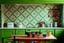 10 an eclectic kitchen with bold green cabinets, bright printed tiles on the backsplash, a wooden table and a chair plus colorful tableware