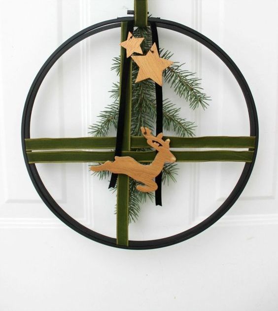 a modern Christmas wreath of an embroidery hoop, green and black velvet ribbons, evergreens, wooden stars and a deer