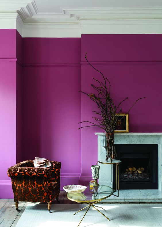 a magenta to hot pink space with a fireplace, a bold printed chair, a couple of coffee tables and some branches plus artwork