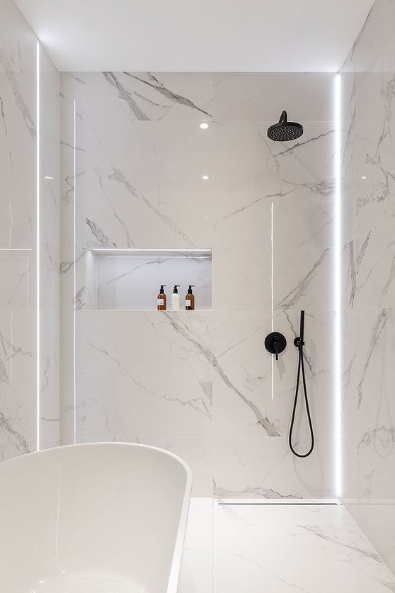A minimalist white bathroom fully clad with marble, with a tub and a shower plus built in lights for a refined feel