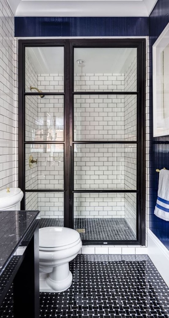 Black and white graphic tiles on the floor, white subway tiles with black grout on the walls in a walk in shower