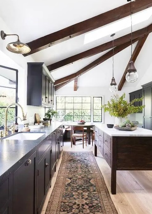A chic modern farmhouse kitchen with a light stained floor, dark wooden beams and a kitchen island that dominate over the space