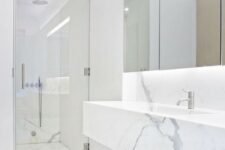 31 a clean minimalist space done with white marble, a mirror with lights, a shower space and a marble vanity