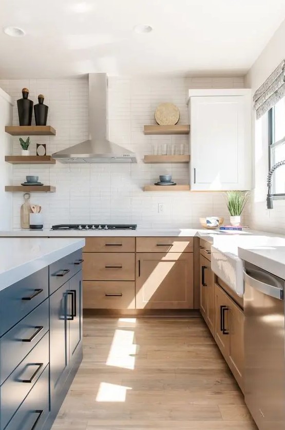 A modern farmhouse kitchen with light stained cabinets, a navy kitchen island, white stone countertops and a skinny tile backsplash, black handles
