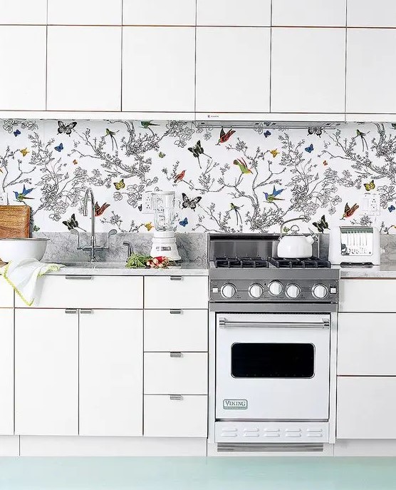 To avoid a boring look in an all white kitchen, rock a colorful wallpaper backsplash with butterflies and birds