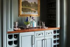 44 a vintage built-in home bar with blue cabinetry, wine storage compartments, artwork, wine bottles and wine glasses