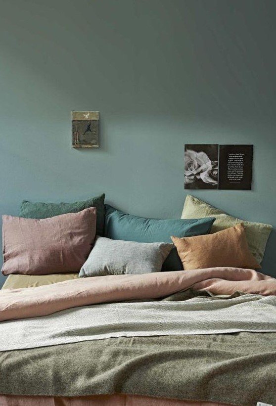 A muted colored bedroom with a dark green wall, pillows of muted shades like rust, greens and mauve