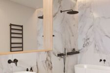 46 a refined white bathroom done with large scale marble tiles, with black fixtures and a large mirror in a wooden frame