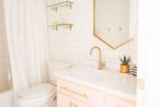 48 a contemporary bathroom clad with white tiles, with a light pink vanity, gold fixtures, knobs and a geometric mirror