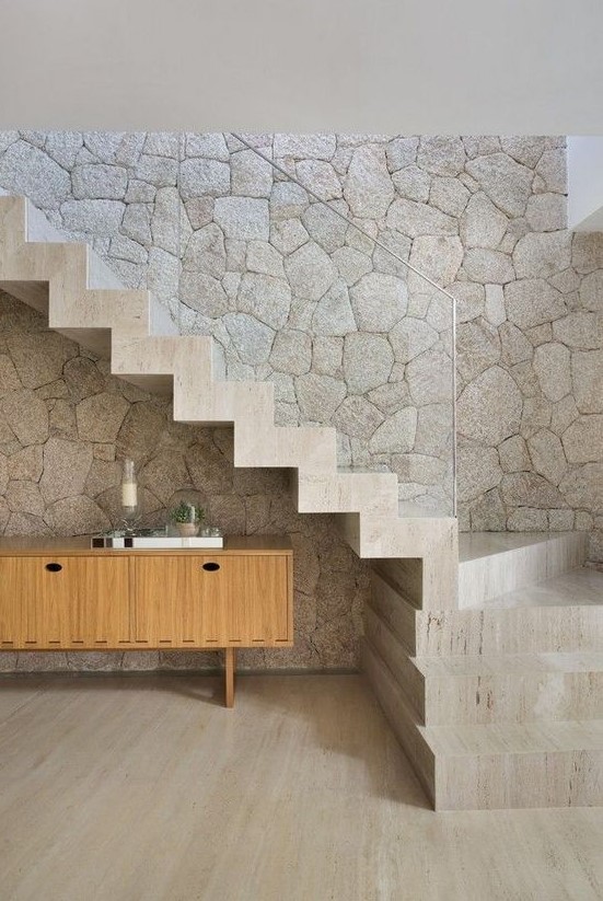 a limestone statement wall and a matching neutral staircase with clear glass railing for an ultimate contemporary space