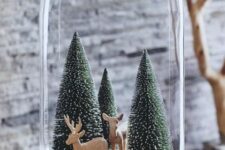 a cloche Christmas terrarium with bottle brush Christmas trees, some logs and deer figurines is ultimately cute