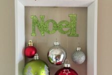 a cool frame Christmas wreath with silver, green and red ornaments, a green letter banner and a red poinsettia on top