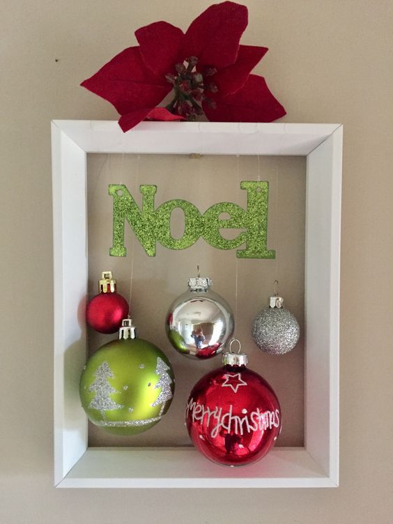 a cool frame Christmas wreath with silver, green and red ornaments, a green letter banner and a red poinsettia on top