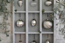 a cool grey Christmas ornament display with mercury glass ornaments and greenery on top is pure elegance