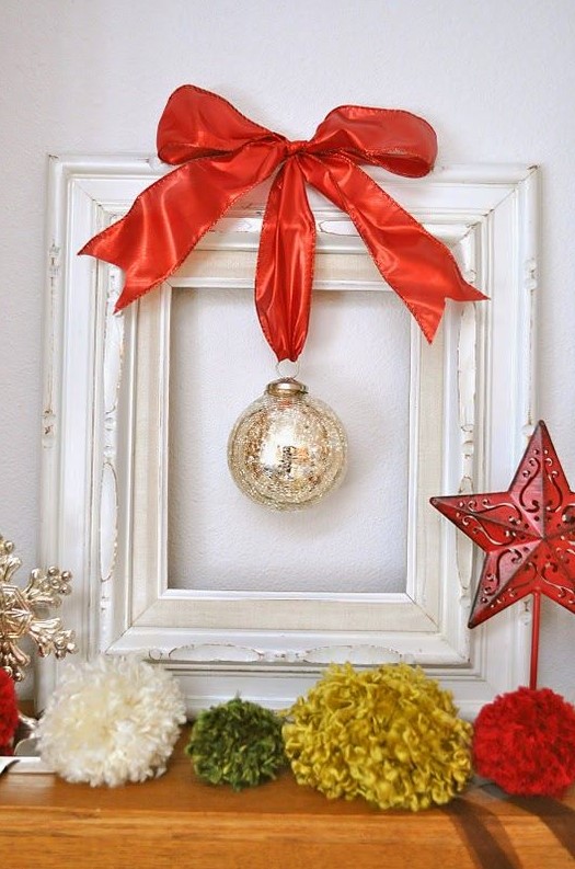 a mini Christmas wreath of a white frame, a single mercury glass ornament and a large red ribbon bow on top
