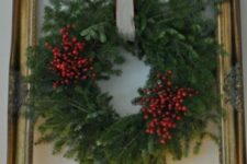 a pretty Christmas decoration – a lush evergreen and berry wreath with a neutral bow attached to an oversized gilded frame