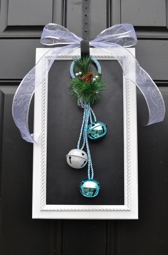 a white picture frame wreath with silver and turquoise bells, evergreens and pinecones and a large sheer bow on top