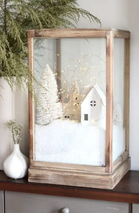 An oversized wooden candleholder with faux snow, mini houses and churches, a mini bottle brush tree and lights