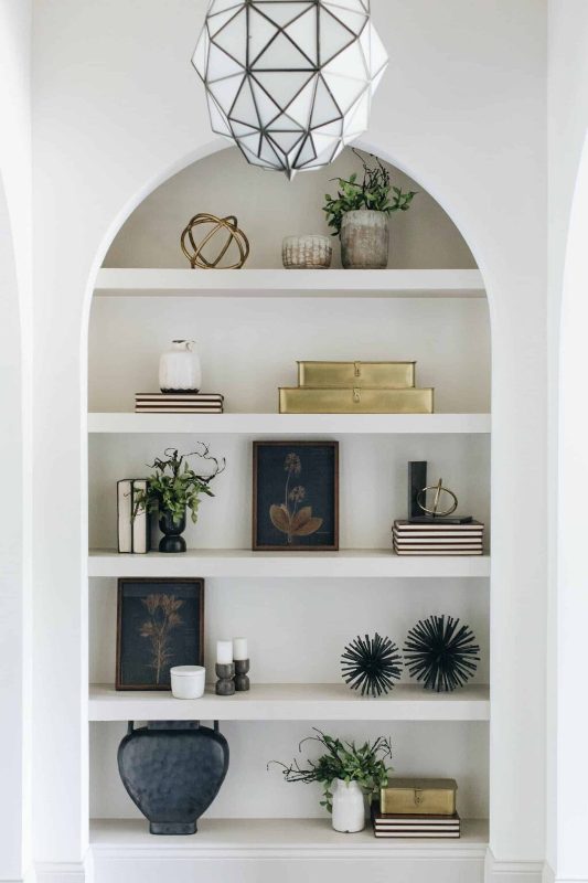A large arched niche with shelves and lots of stuff on display   books, plants, vases and candles is a cool idea