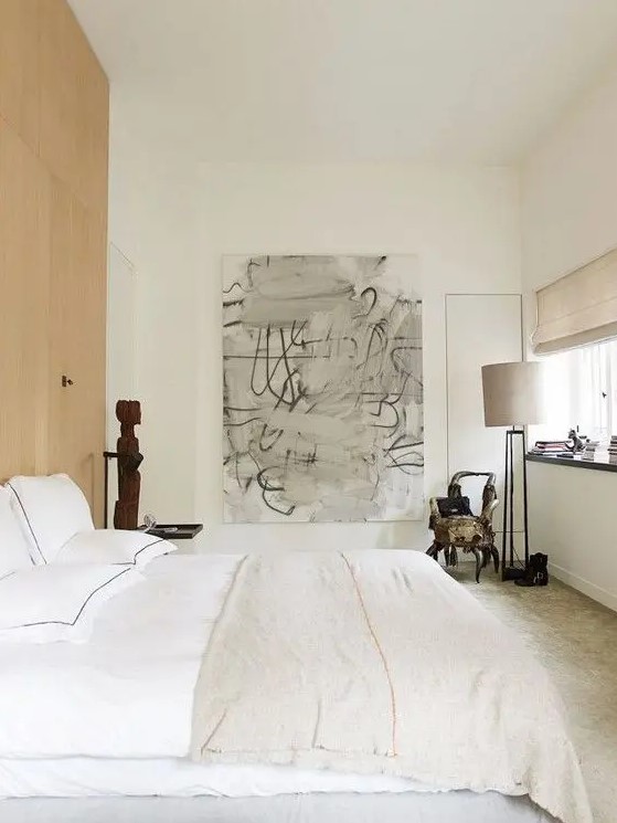 a neutral bedroom with light-colored furniture and lamps, with a wooden accent wall and some bold and dramatic art