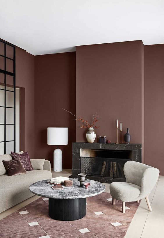 A refined and chic living room with chocolate brown walls, a built in black fireplace, neutral furniture, a black and white table and a burgundy rug