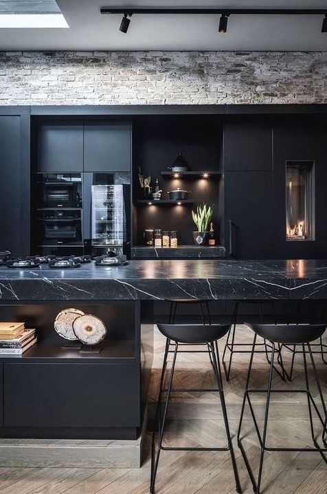 A contemporary black kitchen with a large kitchen island with a marble countertop, built in lights and metal stools