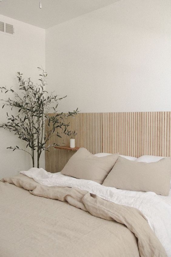 a neutral minimalist bedroom with an extended wood slat headboard, neutral bedding, floating nightstands and a potted plant