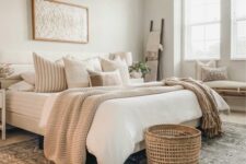 10 a cozy neutral bedroom with a bed and layered bedding, a basket, a printed rug, a bench with pillows and nightstands