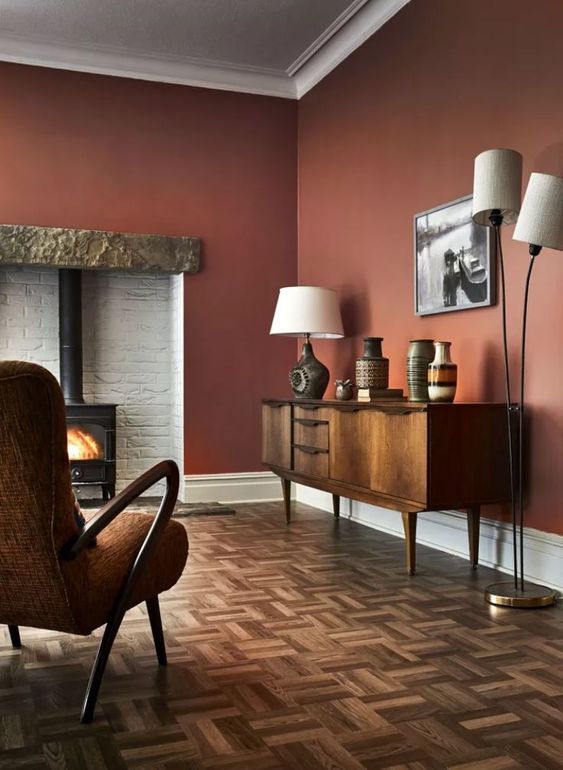 A rich colored living room with burgundy walls, a hearth, a vintage credenza, a floor and table lamp