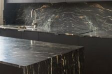 16 a minimalist black kitchen with sleek cabinets, black marble countertops and a backsplash and neutral fixtures