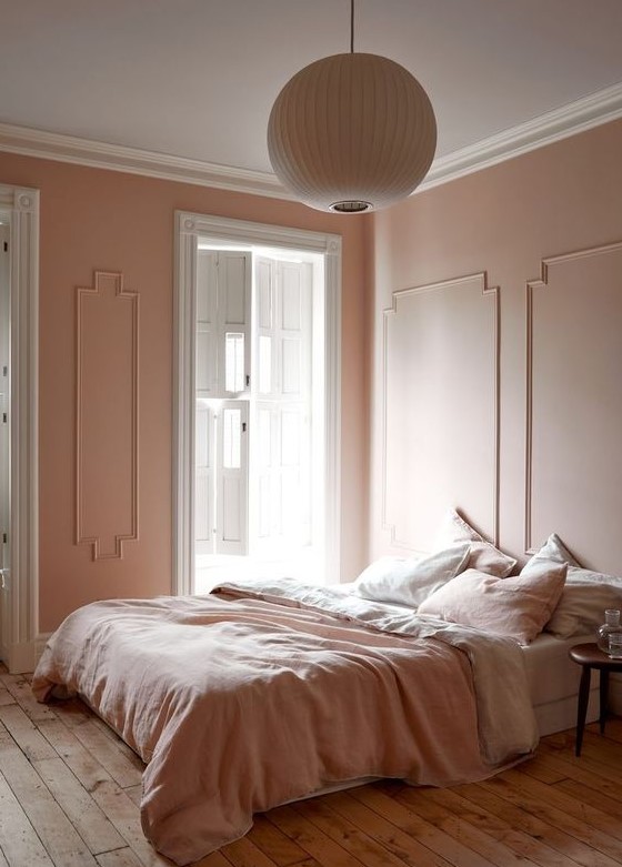 A refined vintage inspired bedorom with blush molding walls, blush and white bedding, a wooden floor and a paper lamp