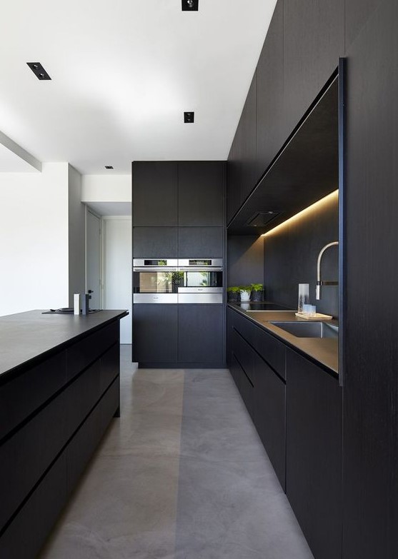 A minimalist black kitchen with sleek cabinets, built in lights, a large kitchen island and built in appliances