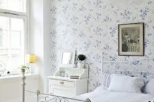17 a vintage-inspired bedroom with a blue floral wall, a white forged bed, white furniture, a dark artwork and a pendant lamp
