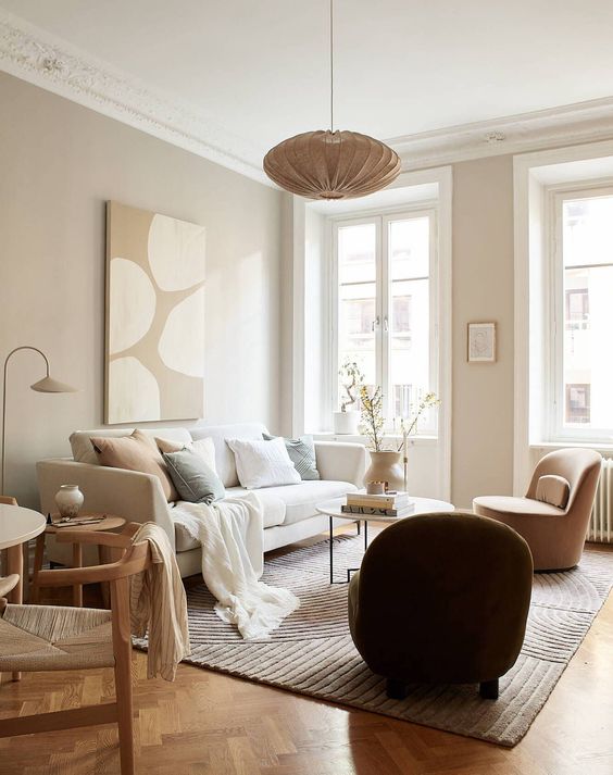 A warm colored neutral living room with greige walls, a creamy sofa with neutral pillows, a tan chair and a side table