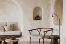 23 a minimalist Mediterranean living room with plaster walls and niches, a built-in sofa in one of them, a neutral chair and some side tables