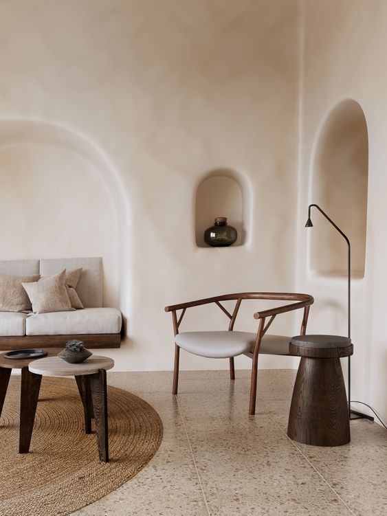 A minimalist Mediterranean living room with plaster walls and niches, a built in sofa in one of them, a neutral chair and some side tables