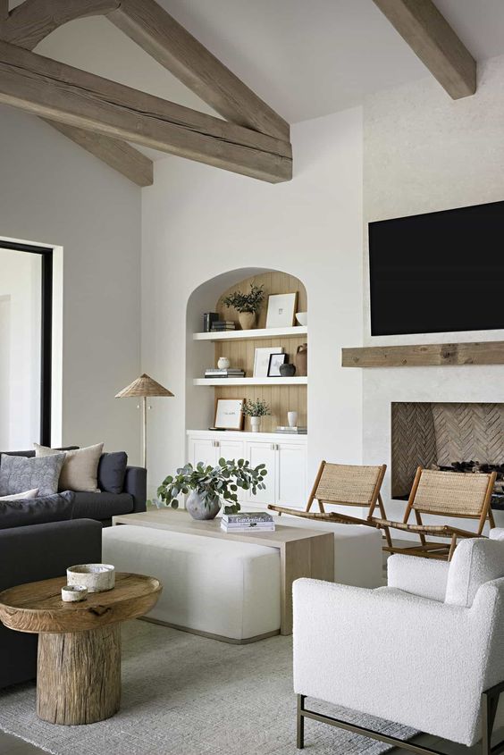 A neutral Mediterranean living room with a niche with shelves and built in storage units, a fireplace, a charcoal grey sofa and creamy chairs and an ottoman