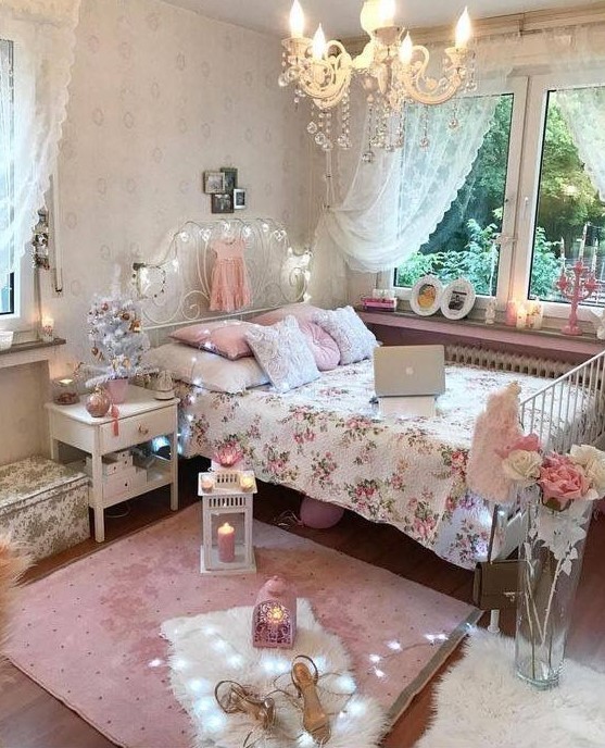 a pink and white shabby chic bedroom with a forged bed, white furniture, pink and floral bedding, candle lanterns and a crystal chandelier